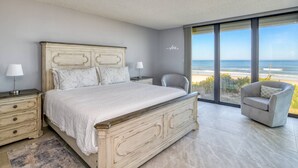 A bedroom with a large bed, bedside tables, a chair, and a view of the beach. - New Flooring, Kitchen, & Bath! Beachfront, Direct Ocean & Pool Views, Elevator, $300 in Free Tickets (St. Augustine)
