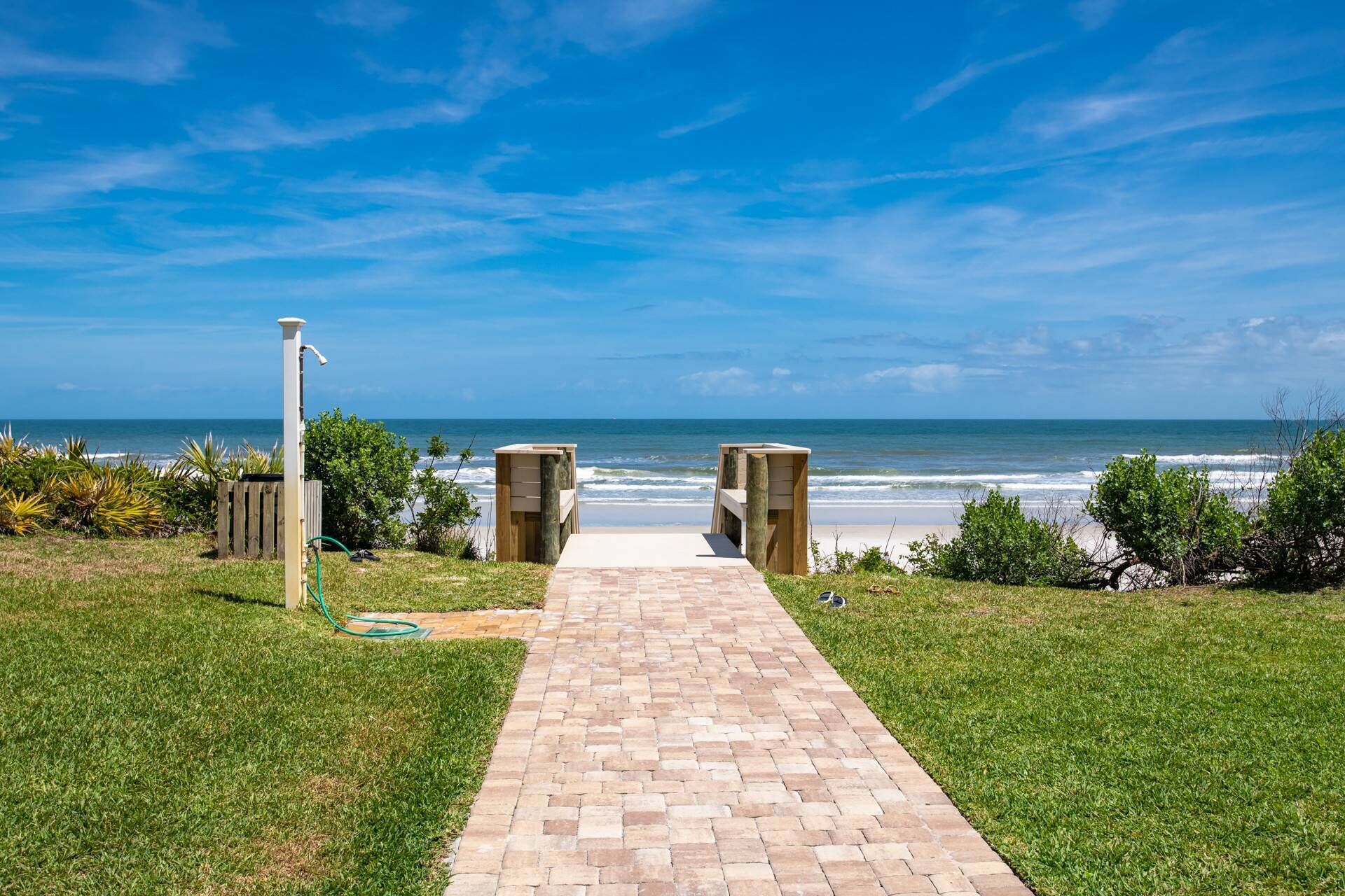 A paved pathway leading to a beach with a clear view of the ocean.