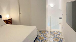 Une chambre d’hôtel avec un lit, une table de chevet, une télévision et une salle de bain dont le sol est recouvert de carreaux décoratifs.