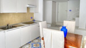 Une cuisine de taille réduite avec des meubles blancs, un évier et un pare-feu en carrelage.