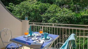 Un balcon avec une table dressée pour le petit-déjeuner, entouré d’une végétation luxuriante.