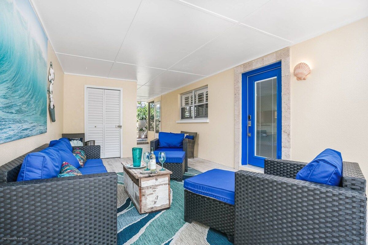 A covered outdoor seating area with wicker furniture and blue cushions, a white door, and a wall-mounted light fixture.