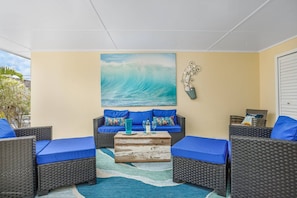 Une pièce baignée de lumière, meublée de meubles en osier, avec une table basse en bois et un grand tableau représentant des vagues accroché au mur.
