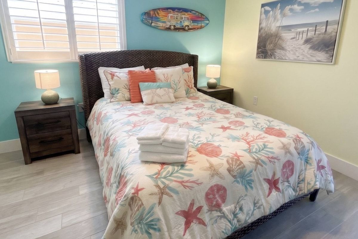 A bedroom with a bed, nightstands, a window, and wall art.