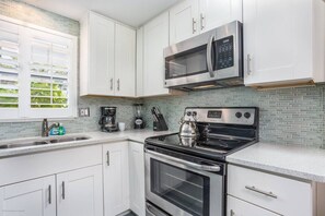 A modern kitchen with white cabinets, a stainless steel microwave, a gas stove, and a coffee maker. - Lounge at Lulu's #2 | 5 Min to Beach | Pool | Dog (Sarasota)