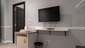 Une petite cuisine équipée d’un réfrigérateur, d’une machine à café et d’une poubelle. Un téléviseur à écran plat est fixé au mur, au-dessus d’une étagère blanche.