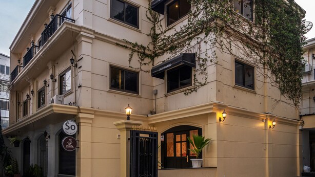 Un immeuble à plusieurs étages, doté d’une façade beige, d’un portail noir et d’une enseigne indiquant qu’il s’agit d’un café.
