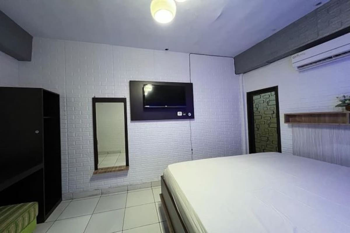 A bedroom with a bed, a TV mounted on the wall, a wardrobe, and a mirror.