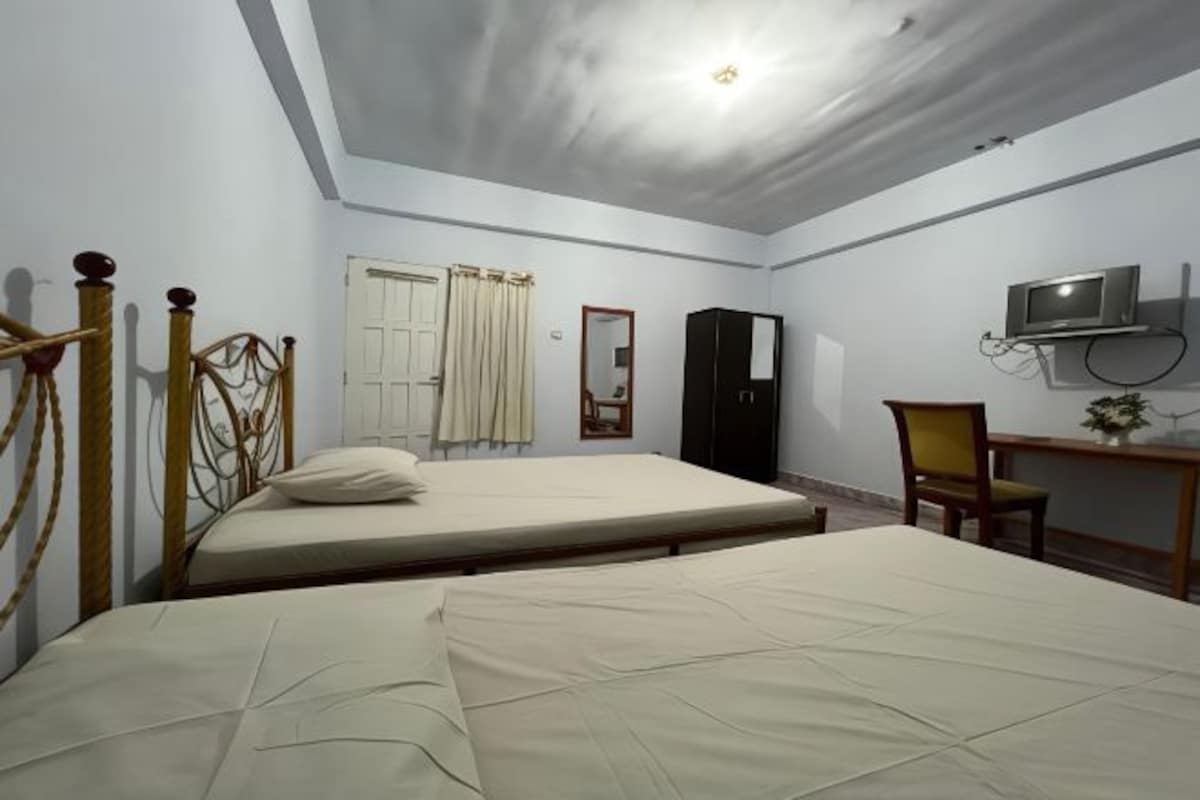A bedroom with two beds, a desk, a chair, a television, and a wardrobe.