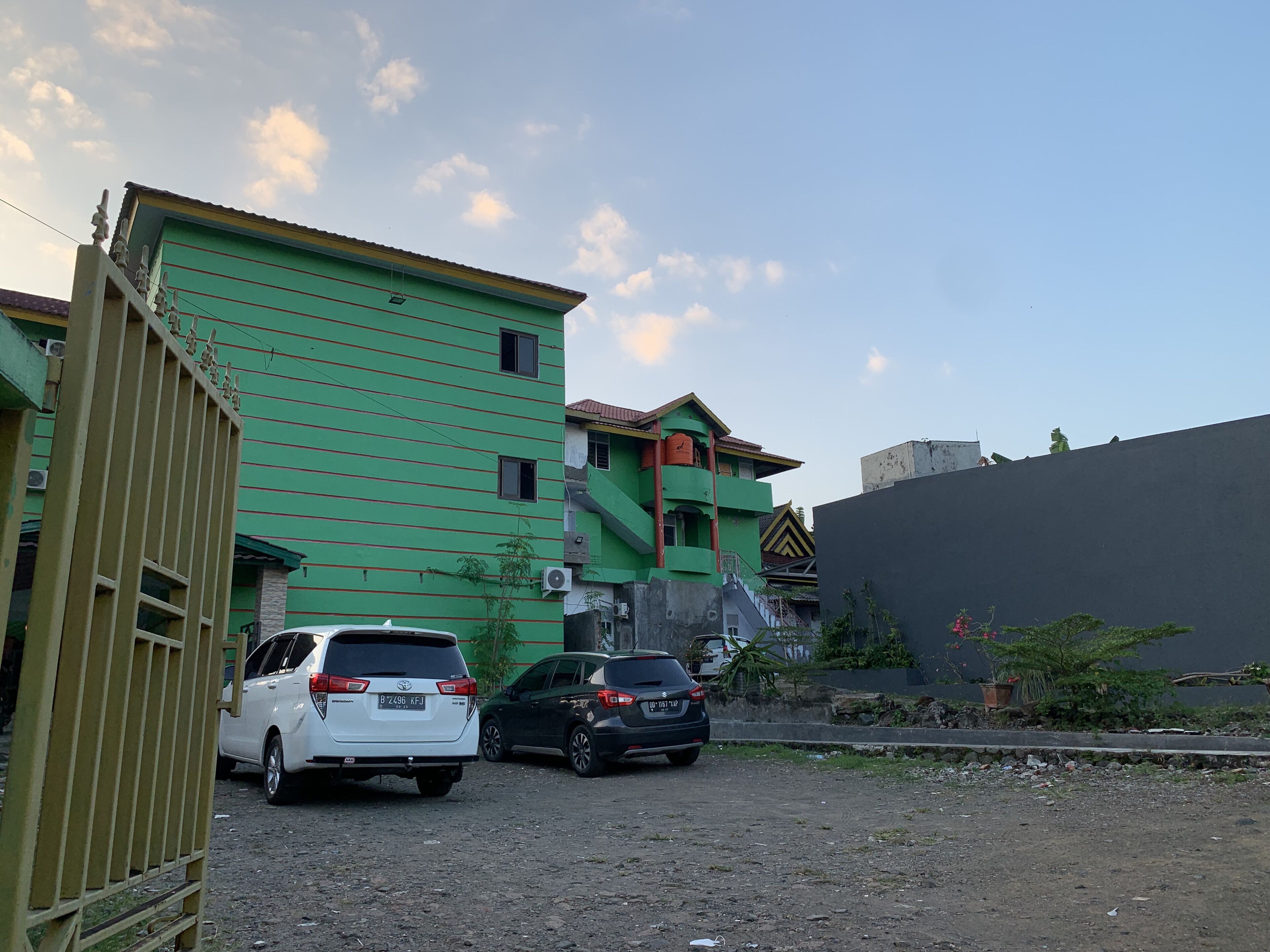 Un espace de stationnement avec deux voitures, un bâtiment vert et un mur gris.