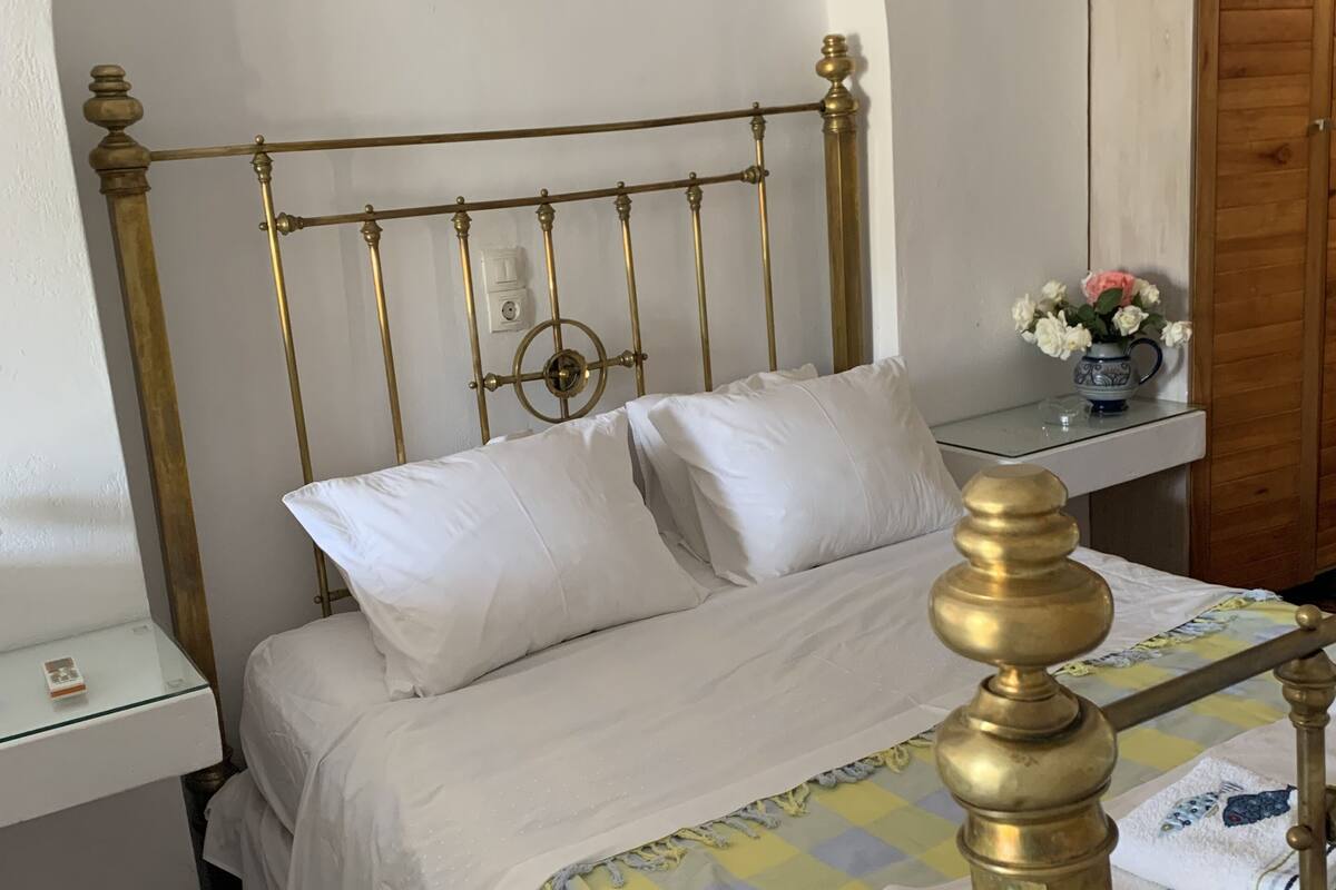 A bed with a gold headboard, white bedding, and a checkered blanket.