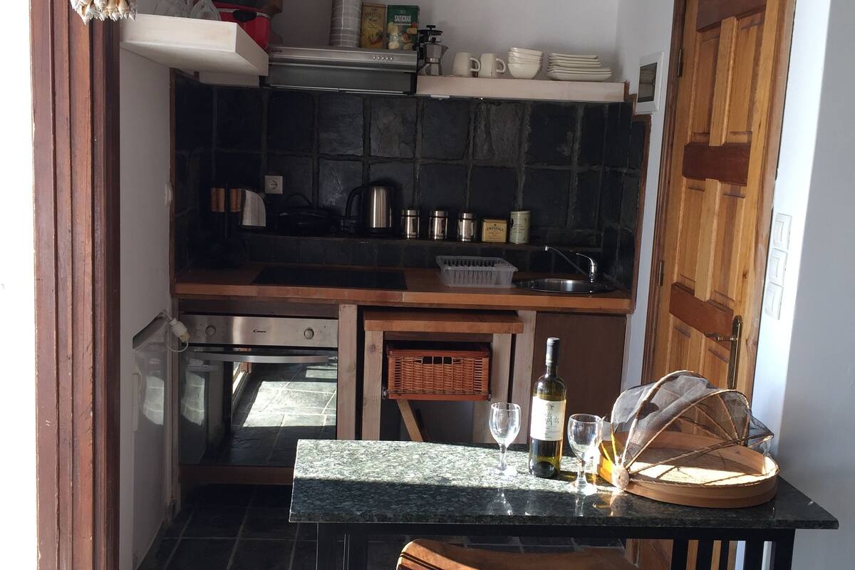 A compact kitchen with a stone backsplash, wooden cabinets, and a countertop with a wine bottle and glasses.
