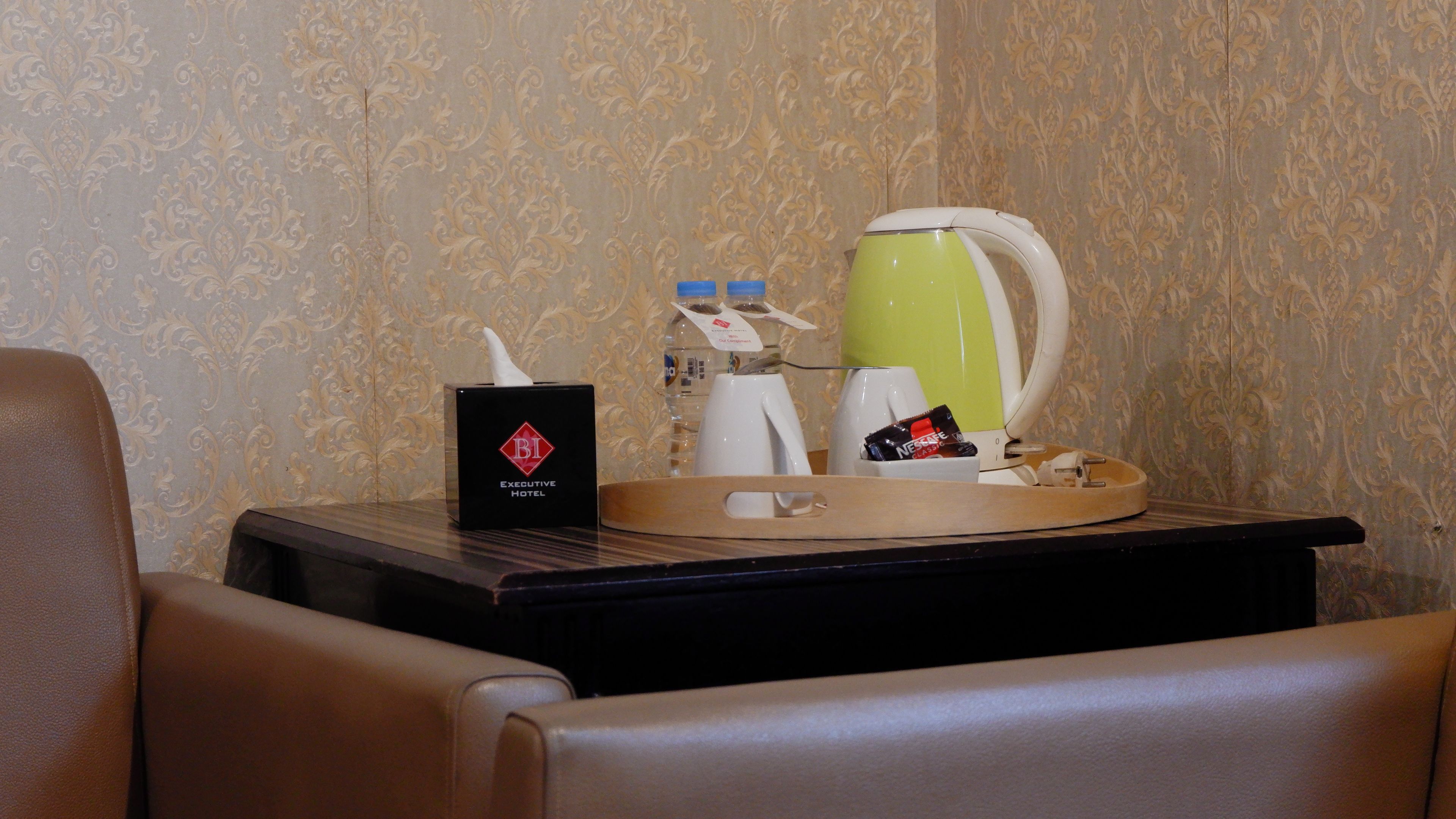 Une chambre d’hôtel équipée d’un minibar, d’un plateau avec une cafetière, une bouteille d’eau, une boîte de mouchoirs et une tasse de café.