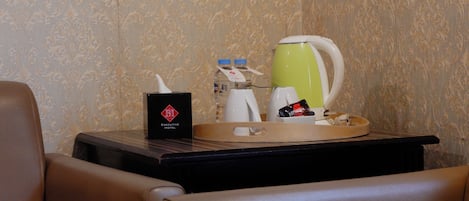 Habitación de hotel con minibar, bandeja con cafetera, botella de agua, caja de pañuelos y taza de café.
