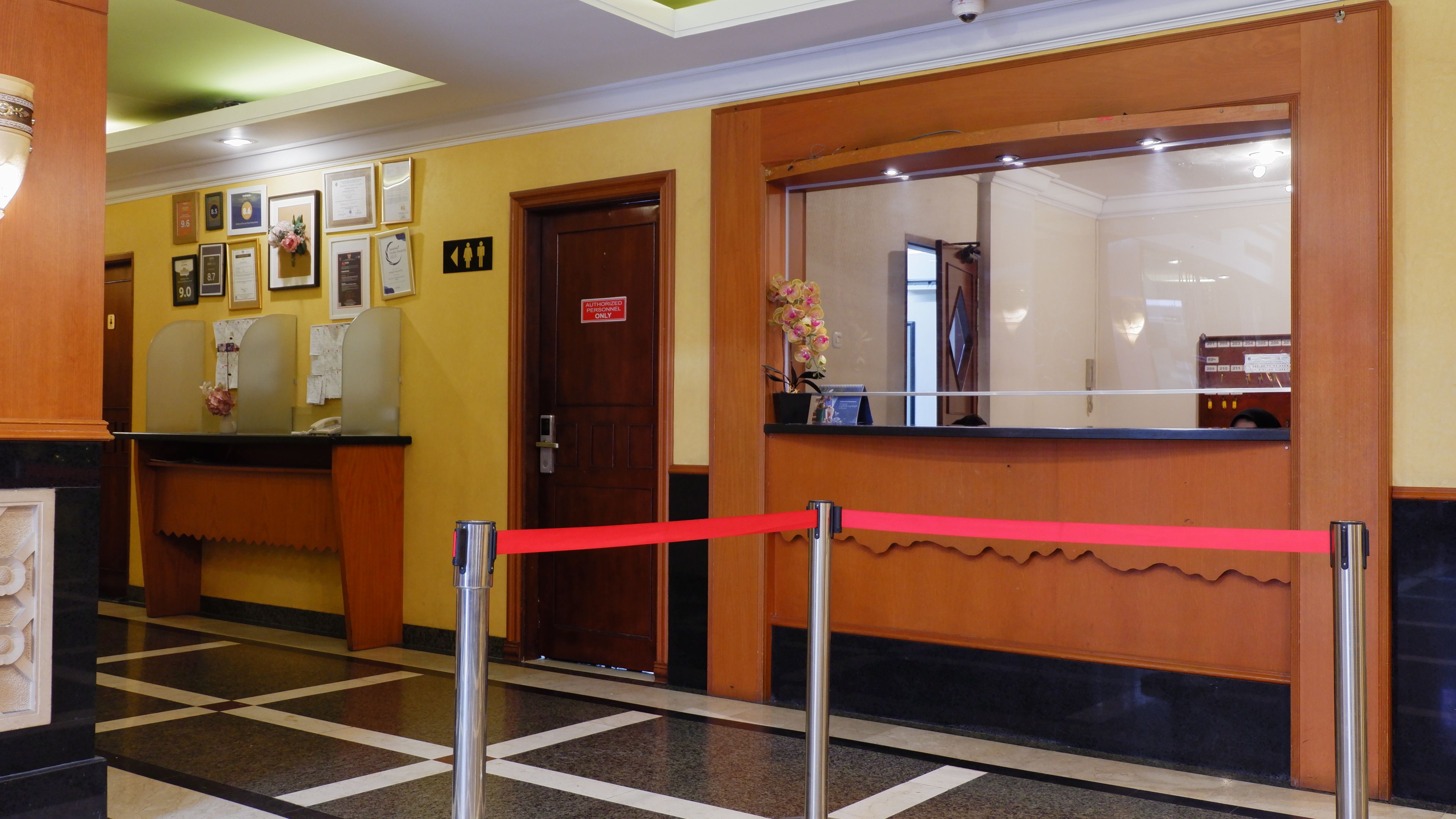 Un área de recepción con mostrador, una puerta de madera y una barrera de cuerda roja.