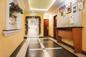 A hotel lobby with a reception desk, a decorative statue, a Christmas wreath, and a tiled floor.