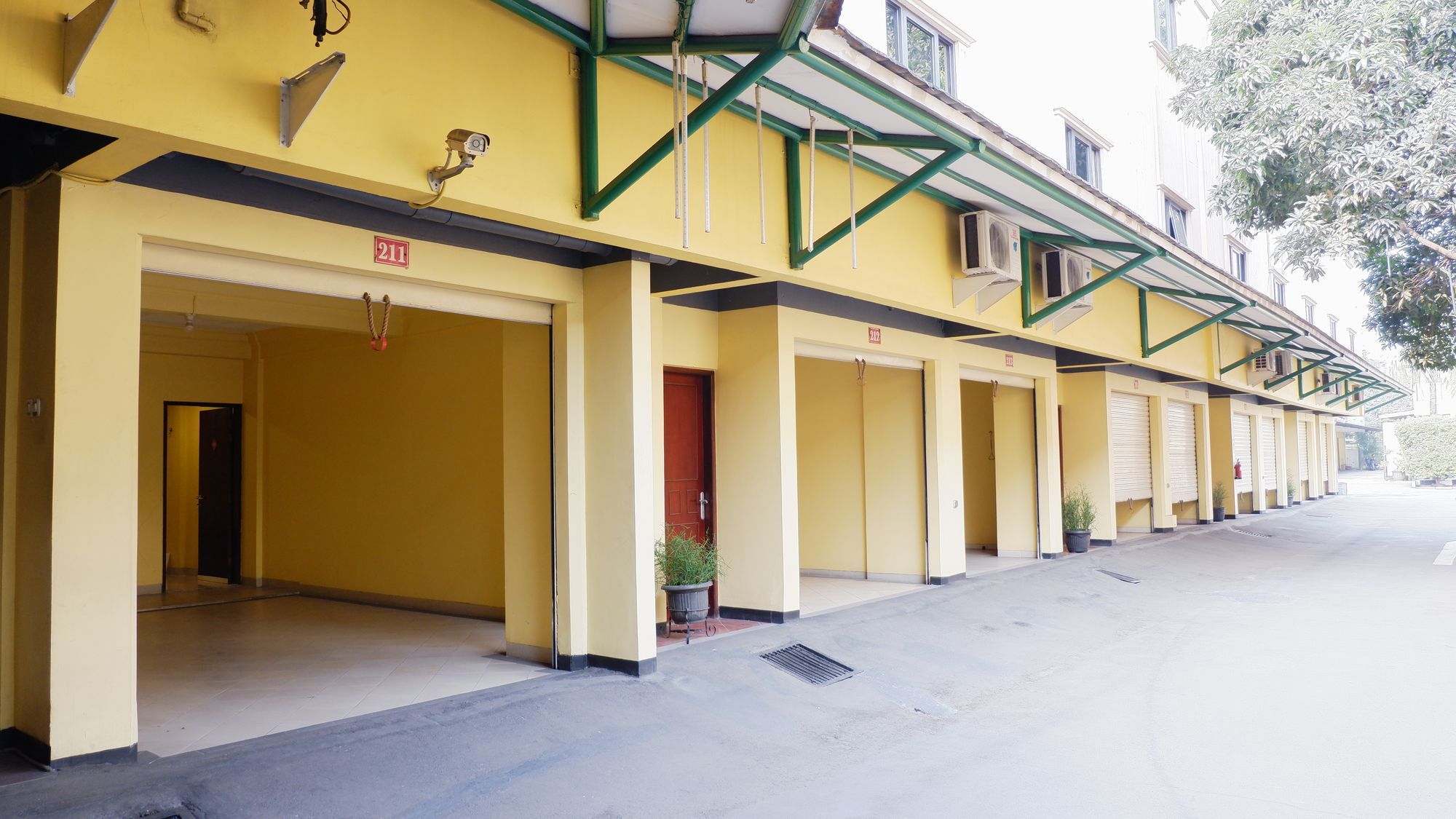 Fila de habitaciones de hotel amarillas con puertas numeradas, una cámara de seguridad y un extintor.