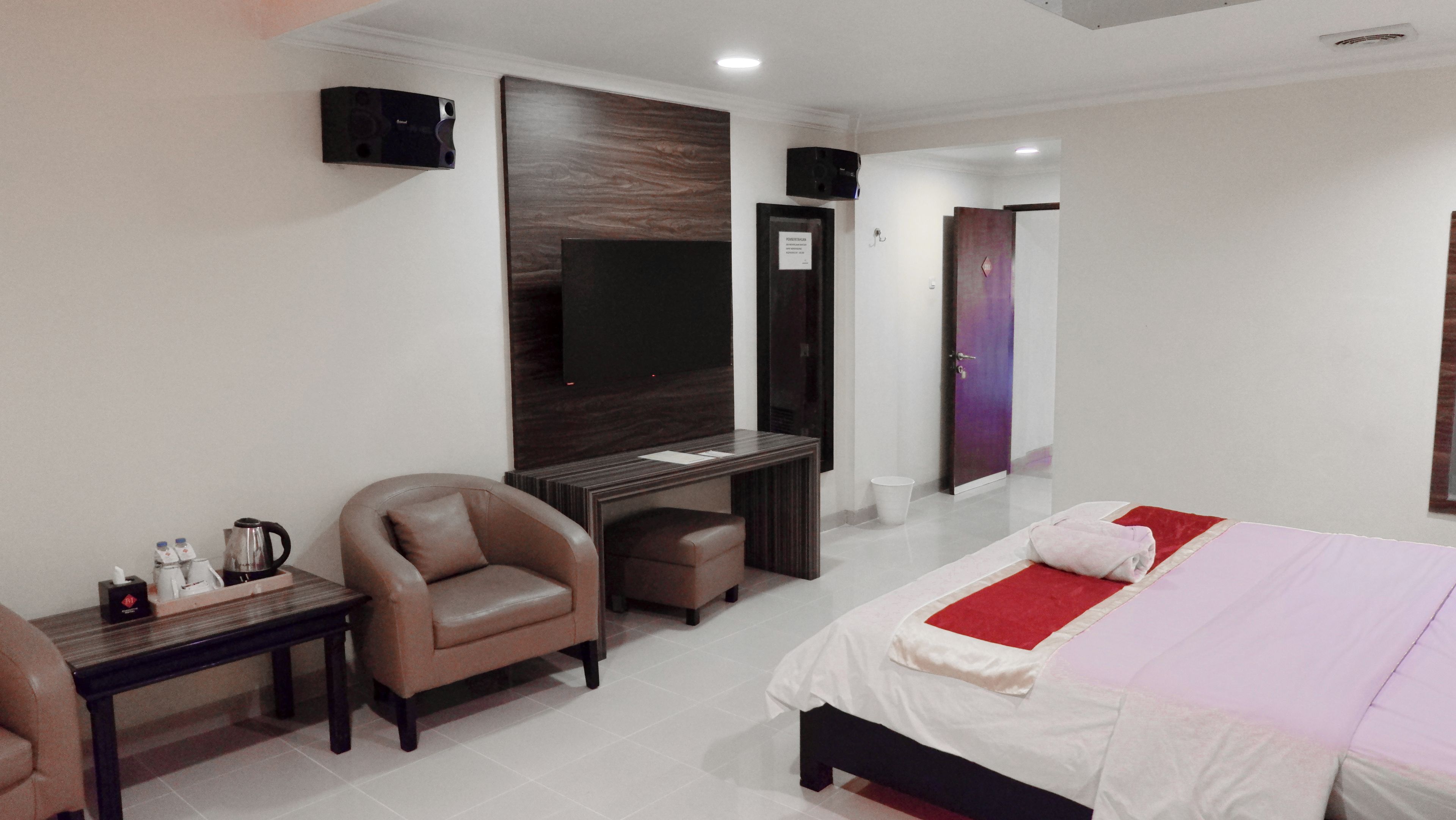 Habitación de hotel con cama, escritorio, silla, televisión y puerta.