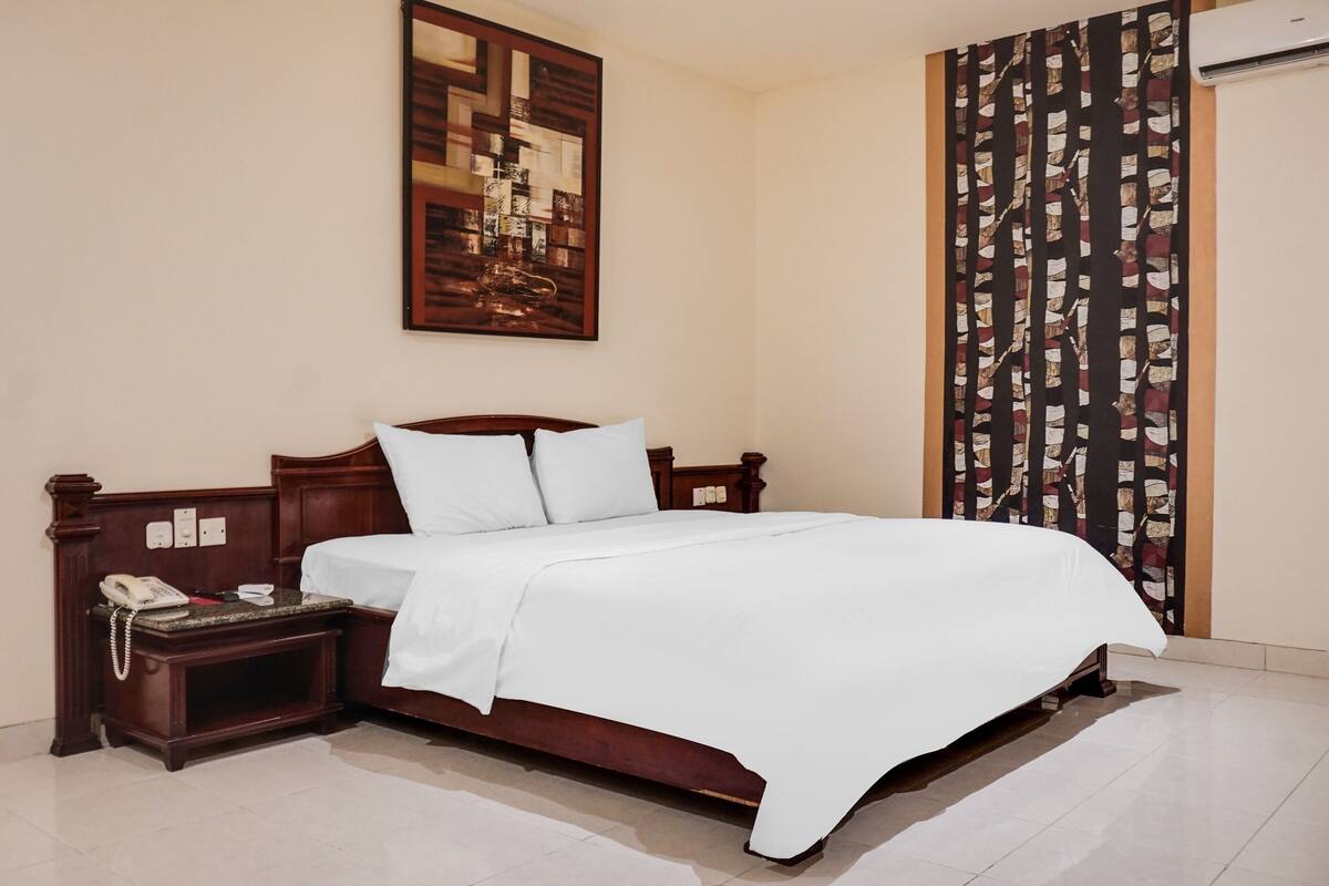 A neatly made bed with white linens, a wooden headboard, and a bedside table with a telephone.