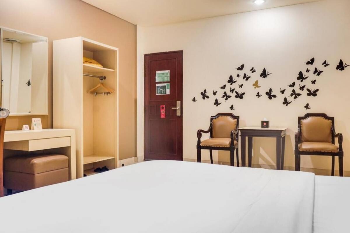 A hotel room with a bed, a wardrobe, a desk, two chairs, and a wall with butterfly decals.