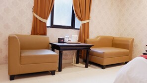 Habitación de hotel con dos sofás de cuero, una mesita con cafetera y un ventanal con cortinas.