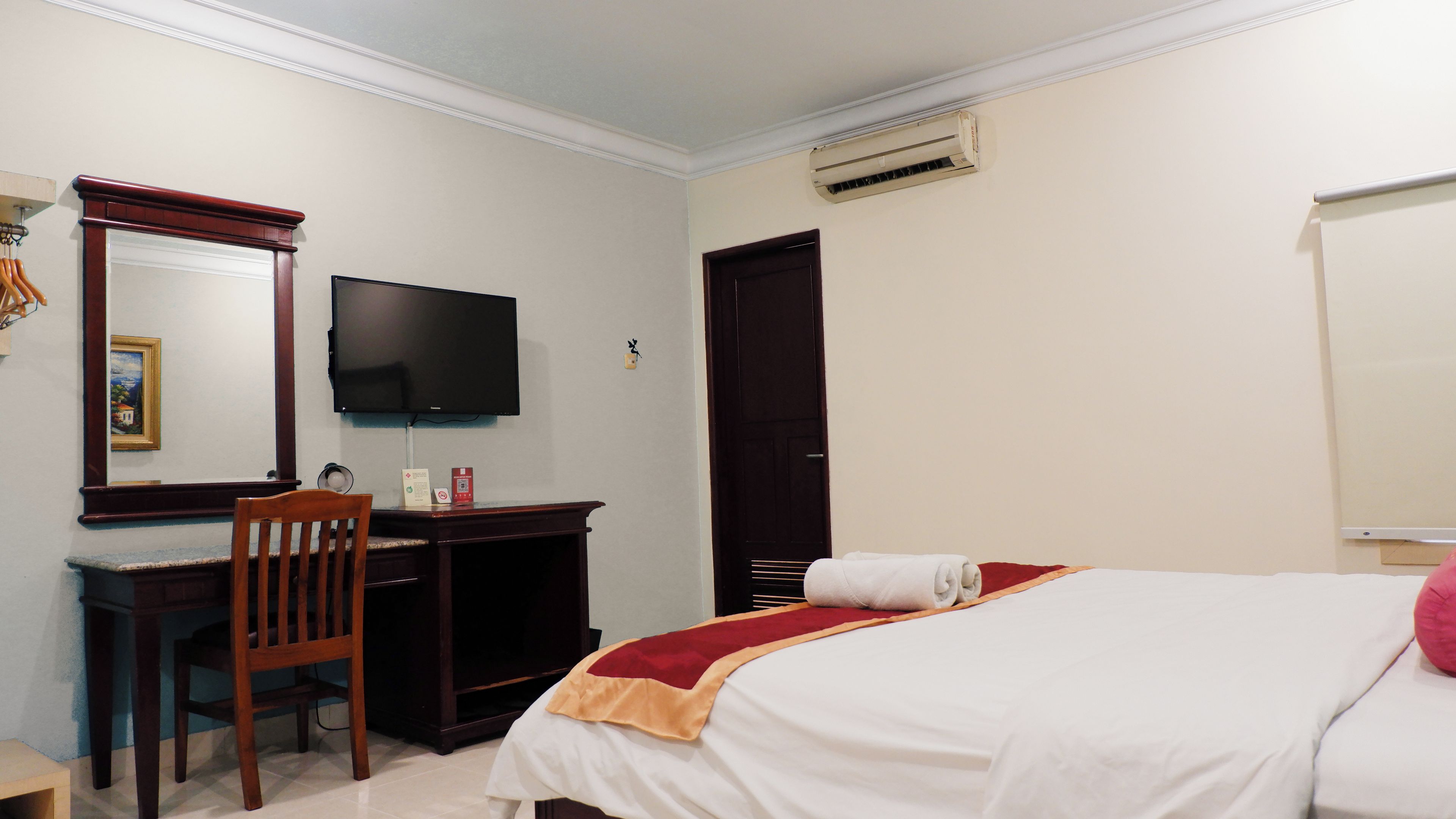A hotel room with a bed, a desk, a chair, a television, and a door.
