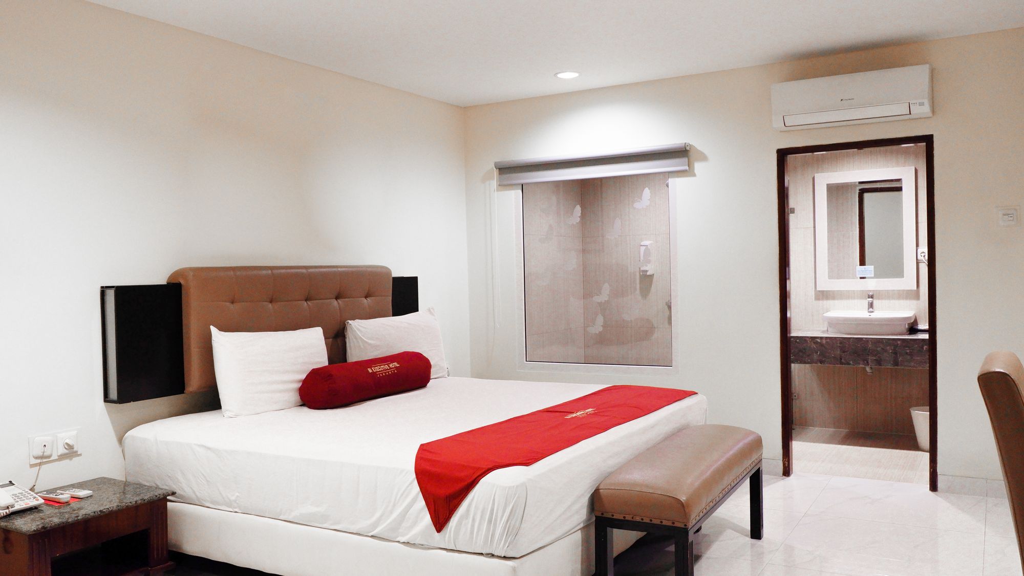 Een hotelkamer met een bed, nachtkastje en een badkamer met wastafel en spiegel.