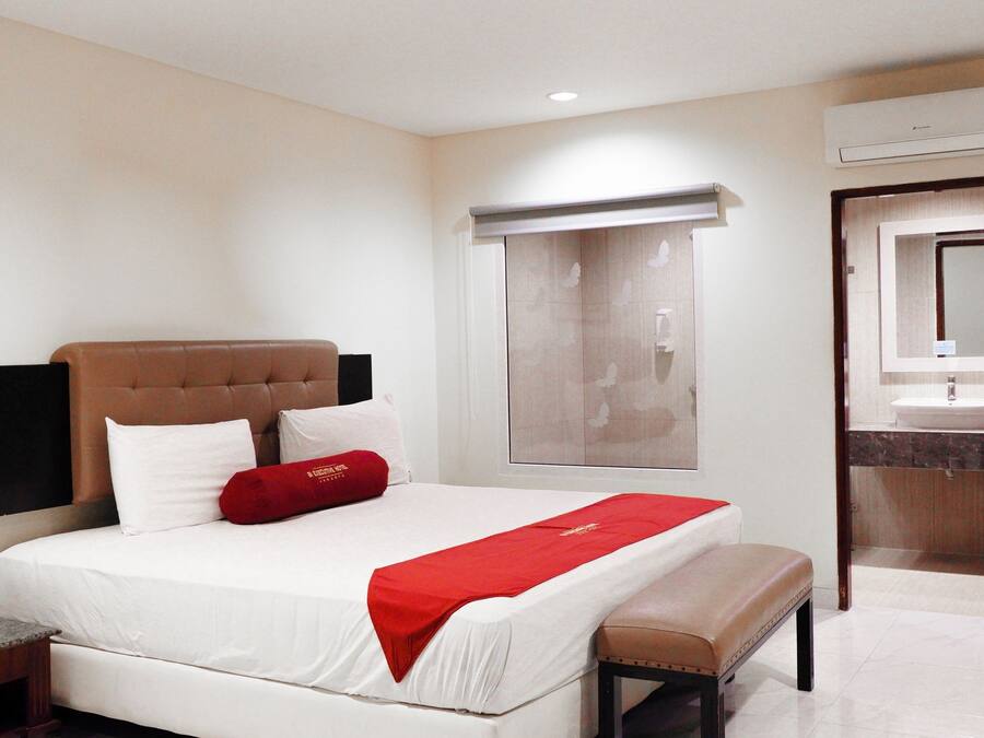 Una habitación de hotel con una cama, mesita de noche y baño con lavabo y espejo.