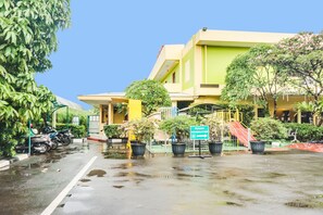 A building with a green and yellow facade, a sign indicating a medical facility, and a wet street suggesting recent rain.