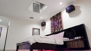 Ein Schlafzimmer mit einem Bett, einer Deckenleuchte, einem Wandlautsprecher und einem Fenster.