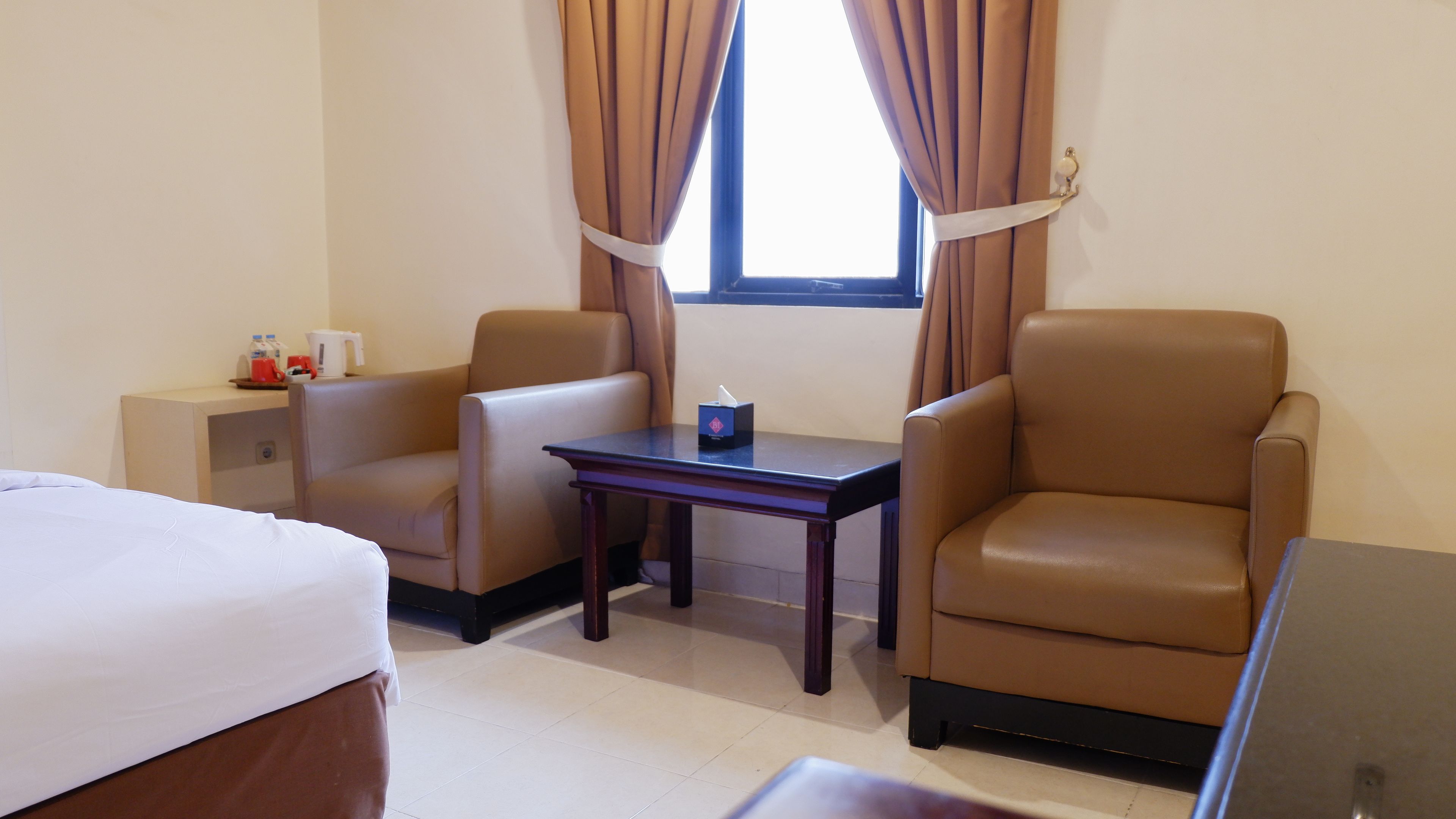 A hotel room with a bed, two armchairs, a small table, and a window with curtains.