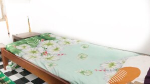 A single bed with a floral bedspread, a nightstand, and a wall-mounted shelf with various items. - Hotel O Desa Wisata Tunggul ArumNearWisata Tunggularum (Kaliurang)