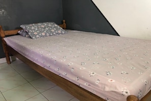 A single bed with a floral-patterned bedspread and a matching pillow in a room with a dark wall and a sloped ceiling.