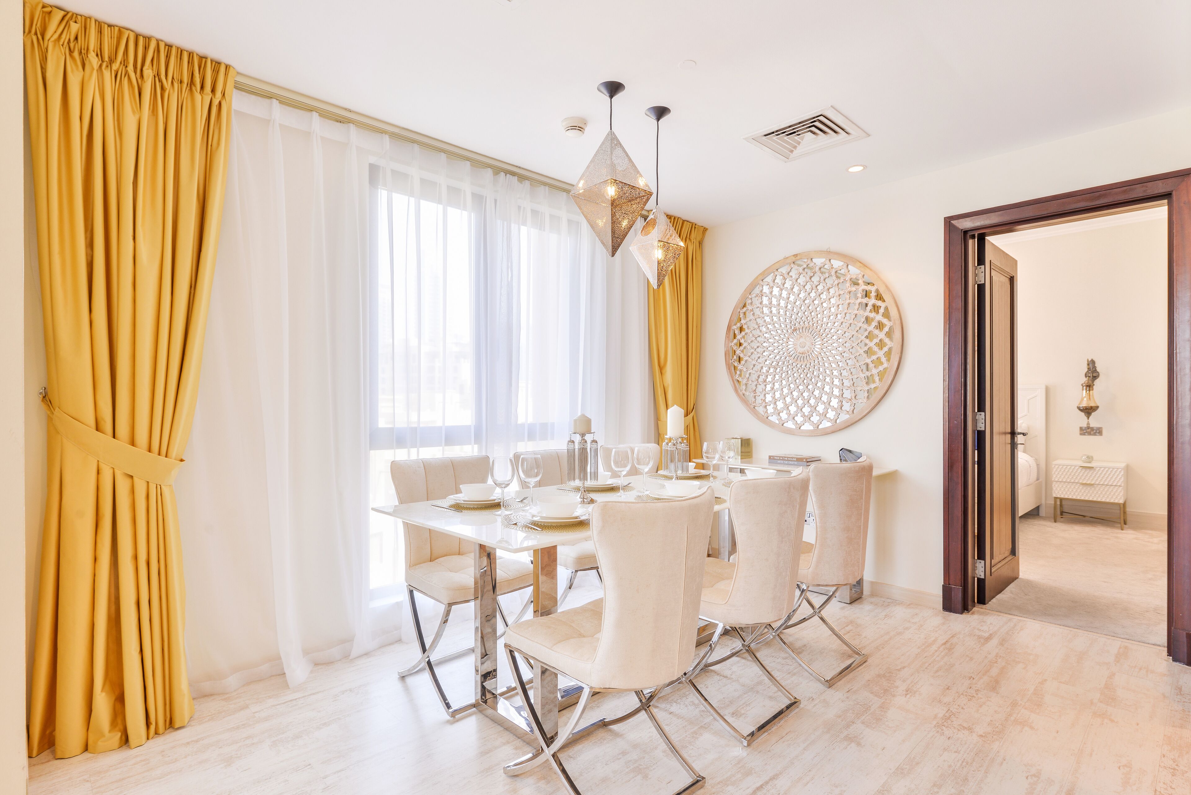 A dining area with a table set for four, a chandelier, and a decorative wall piece.
