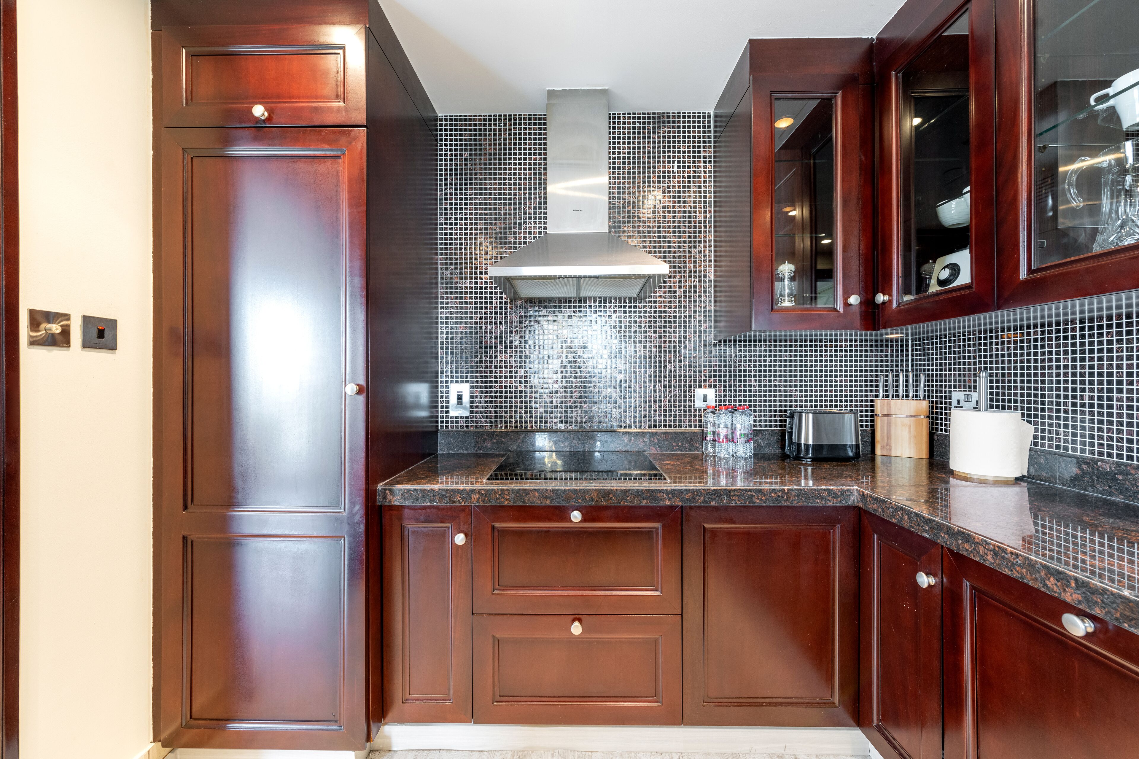 A kitchen with dark wooden cabinets, a stainless steel range hood, and a tiled backsplash.