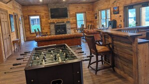 A cozy room with a foosball table, leather seating, a fireplace, and a bar area.