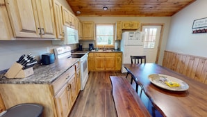 A kitchen with wooden cabinets, a granite countertop, a dining table, and a bench.