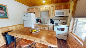 A kitchen with wooden cabinets, a microwave, a stove, and a dining table with a basket of fruit. - PA Grand Canyon, Mountain View, Pine Creek (Gaines)