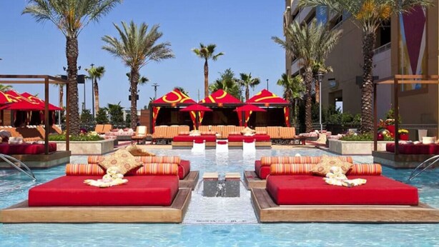 A pool area with red loungers and umbrellas, surrounded by palm trees and a building with a red and yellow logo. - Alluring #A 1 Queen & courtyard by Fremont Str (Las Vegas)