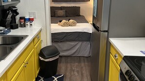 A compact kitchenette with a refrigerator, stove, and sink. A bed with rolled towels and pillows is visible through an open door. - Alluring #A 1 Queen & courtyard by Fremont Str (Las Vegas)