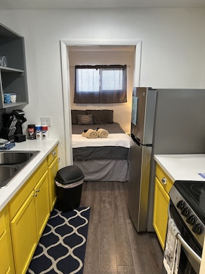 A compact kitchenette with a refrigerator, stove, and sink. A bed with rolled towels and pillows is visible through an open door. - Alluring #A 1 Queen & courtyard by Fremont Str (Las Vegas)