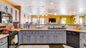 A modern kitchen with grey cabinets, a black stove, a built-in oven, a dishwasher, and a large island with a sink.