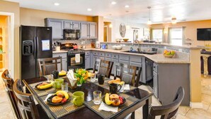 A modern kitchen with a dining area, featuring a black refrigerator, grey cabinets, and a central island with a sink.