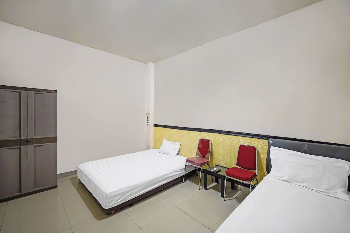 Ein Hotelzimmer mit zwei Betten, einem Kleiderschrank, einem kleinen Tisch und zwei roten Stühlen.