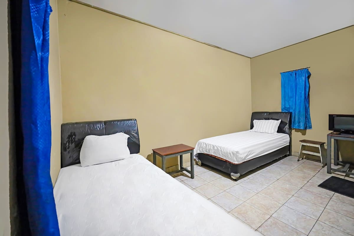 Ein Hotelzimmer mit zwei Betten, einem kleinen Tisch, einem Fernseher und einem Vorhang.