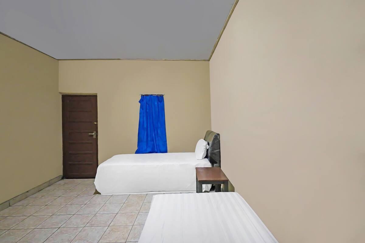 Ein Zimmer mit zwei Betten, einem kleinen Tisch, einer Tür und einem blauen Vorhang.