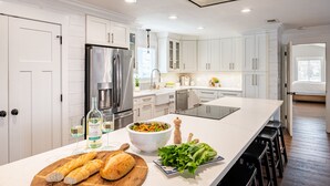 A modern kitchen with white cabinetry, a large island, a refrigerator, and a dining area with stools. - Harborside by AvantStay | Expansive Destin Retreat (Destin)