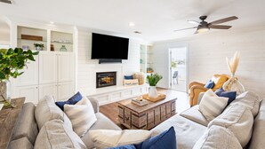 A modern living room with a fireplace, a flat-screen TV, and a ceiling fan. - Harborside by AvantStay | Expansive Destin Retreat (Destin)