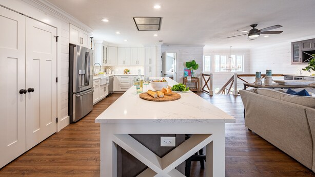 A modern kitchen with white cabinetry, a central island, and a dining area with a sofa and table. - Harborside by AvantStay | Expansive Destin Retreat (Destin)