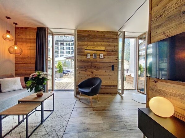 A modern living room with a sofa, a black chair, a coffee table, and a TV mounted on the wall.